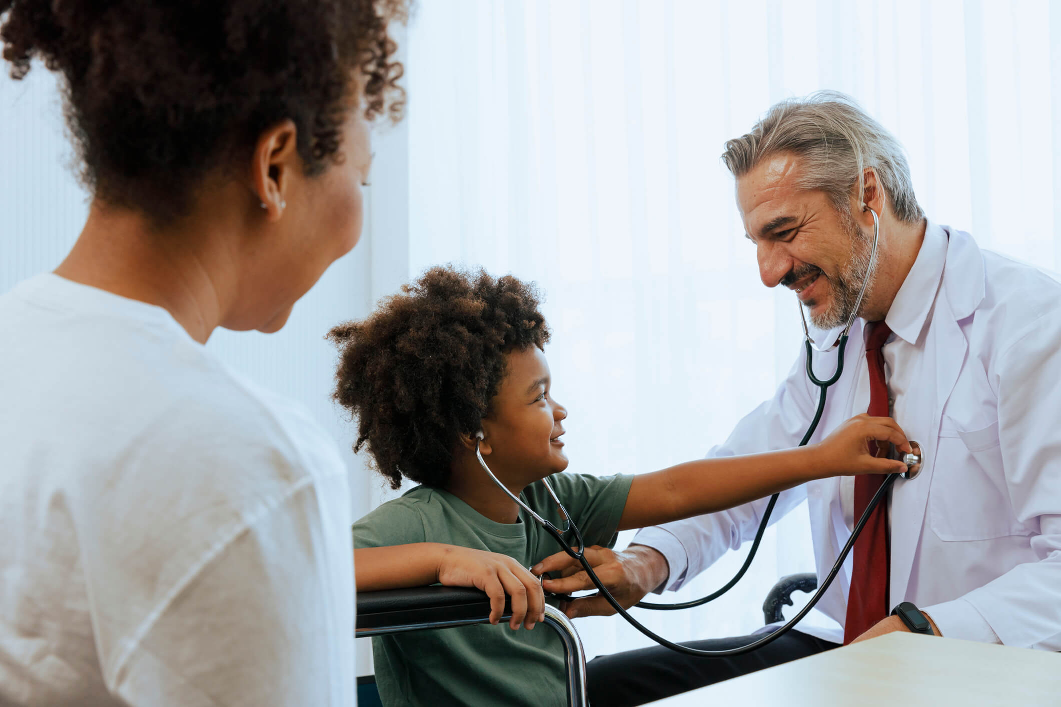 Mother watching young boy use stethescope on doctor