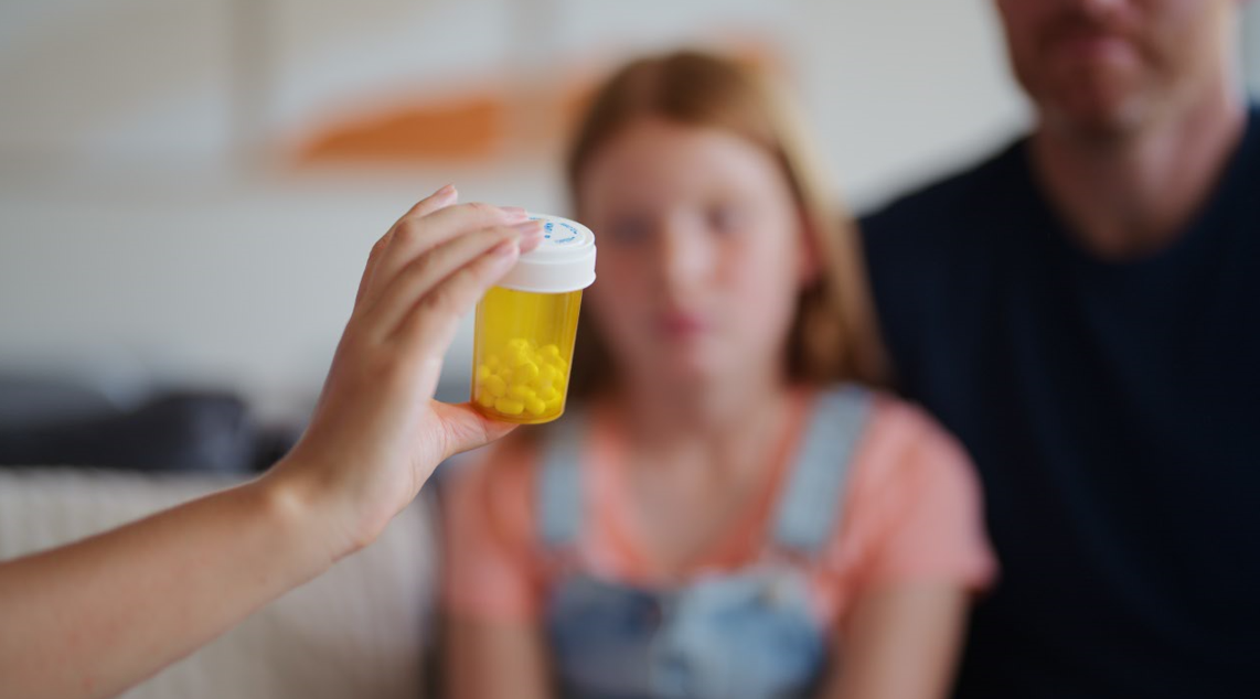 Doctor showing prescription bottle to girl and her father