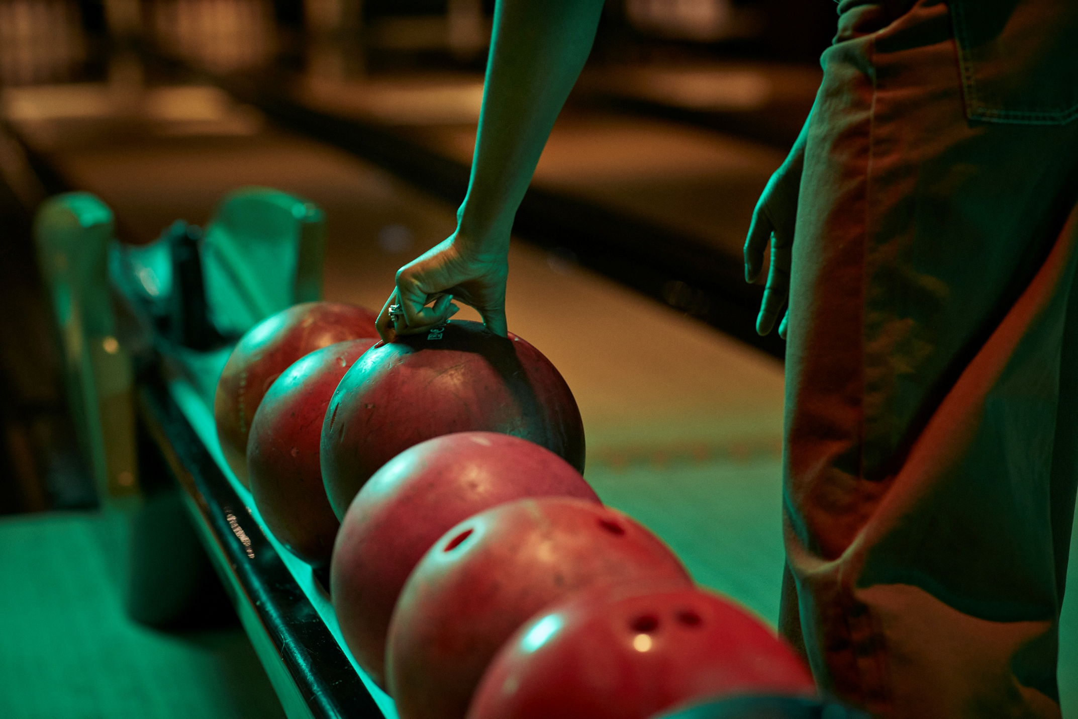 Woman picking up bowling bowl at bowling alley