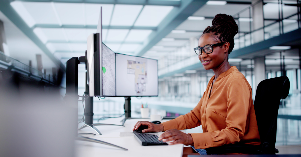 Sunshine Health Works logo on photo of Young woman in an office working a a desk with mutliple computer screens.