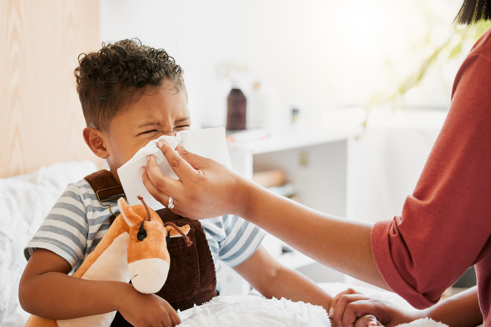 Toddler sneezing into tissue held by his mother.
