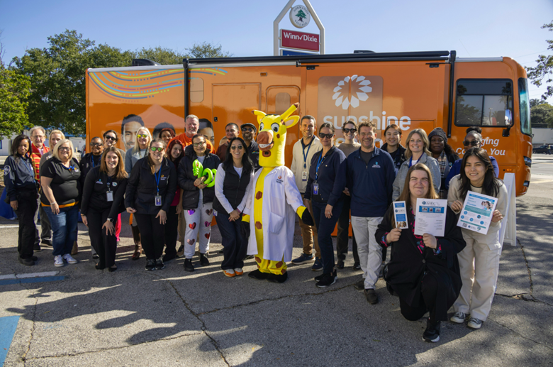 A group of Sunshine Health staff members pose in front of the Sunshine Health Mobile Clinic at event in Jacksonville, Florida.